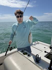 A young angler proudly displaying a freshly caught fish while fishing on a boat in clear waters.