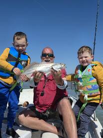 A proud moment as a family celebrates catching a large Speckled Trout while fishing together on a sunny day.