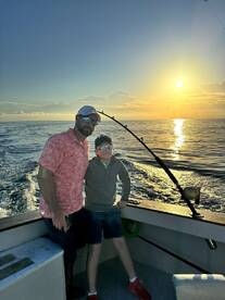 A father and son enjoying a fishing trip at sunset, with a fishing rod in the background, capturing a memorable moment on the water.