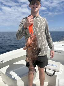 Young angler proudly holding a large Grouper while fishing offshore, showcasing a successful catch.