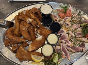 A beautifully arranged platter featuring fried fish fillets and seared tuna, served with various dipping sauces, ideal for a seafood feast.
