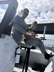 A young boy and an adult proudly displaying a Speckled Trout while fishing on a boat, showcasing a fun family fishing experience.