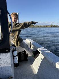 A young angler pointing excitedly while fishing from a small boat, enjoying a day on the water.