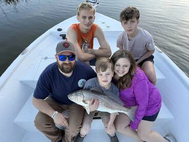 A family enjoying a successful fishing trip, showcasing a large Redfish on a boat.