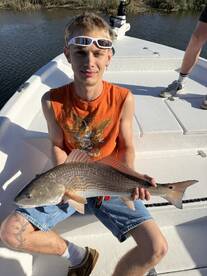 Young angler proudly displaying a Redfish on a boat in a scenic fishing environment.