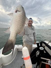 Angler proudly displaying a large Snapper while fishing on a boat, showcasing a successful day on the water.