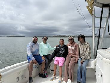 A family enjoying a day on the boat, seated comfortably with a scenic view of the water in the background.