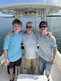 A group of three anglers enjoying a day on the water, posing inside the boat with a scenic backdrop.