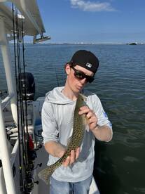 Young angler proudly displaying a Spotted Seatrout while fishing on a boat in calm waters.