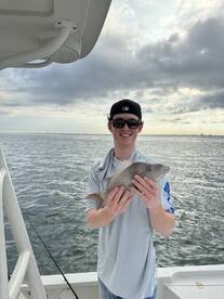A young angler proudly displaying a Snapper while fishing on a boat, with a scenic ocean backdrop.