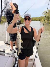 A smiling angler proudly displays a Snook while fishing on a boat in a mangrove area.