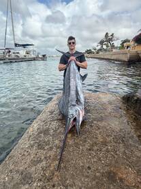Angler proudly displaying a large Marlin at the dock after a successful fishing trip.