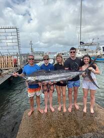 A family proudly displays a large Marlin at the dock after a successful fishing trip.