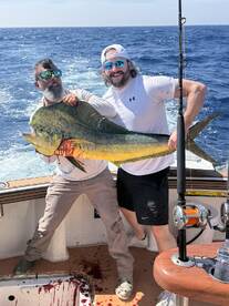 Two anglers proudly displaying a large Mahi Mahi aboard a fishing boat, showcasing a successful deep-sea fishing trip.