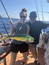 A proud angler holding a vibrant Mahi Mahi while fishing offshore, accompanied by a fellow angler on a sunny day.