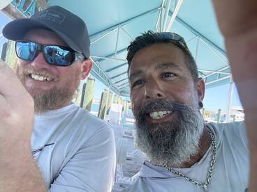 Two anglers taking a selfie under a shaded area, likely at a fishing dock.