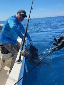 An angler is actively reeling in a large sailfish while fishing in deep blue waters, showcasing the thrill of sport fishing.