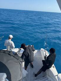 Three anglers actively fishing on a boat in deep blue waters, showcasing the excitement of the catch.