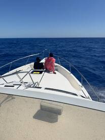 Two individuals enjoying the view from the bow of a boat on a clear day, with the vast ocean stretching out ahead.