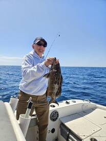 An angler proudly displaying a large Grouper caught while fishing offshore, enjoying a sunny day on the water.
