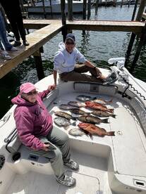 Two anglers relaxing on the boat with a variety of freshly caught fish, including Snapper and Grouper, displayed on the deck after a successful fishing trip.