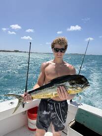 A young angler proudly displaying a large Mahi Mahi while fishing on a sunny day.