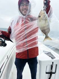Angler proudly displaying a freshly caught fish while wearing a rain poncho on a fishing boat.