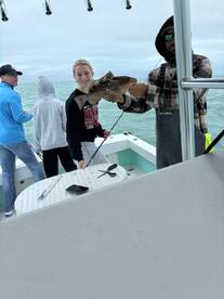 A young angler proudly holds a large grouper while fishing with family on a boat, showcasing a successful catch during their outing.