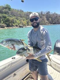 Angler proudly displaying two large Yellowtail fish while on a boat in a scenic fishing location.
