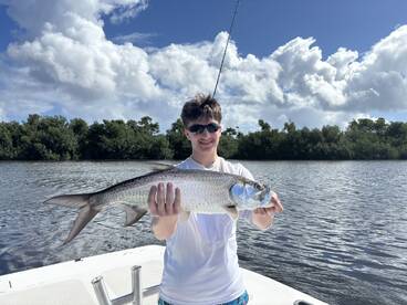 A young angler proudly displaying a large Tarpon while fishing in a scenic mangrove area.