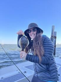 A happy angler proudly displaying a Flounder while fishing from a boat, showcasing a successful day on the water.