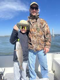 A young angler proudly displaying a striped bass while fishing with an adult on a sunny day.