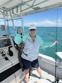 A proud angler holding a flatfish aboard a fishing boat, enjoying a sunny day on the water.