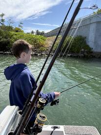 A young angler casting a line from a boat in a scenic waterway, surrounded by lush greenery.