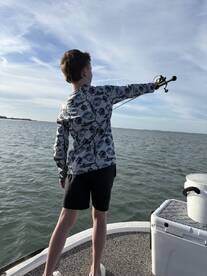 A young angler casting a line from the deck of a boat, enjoying a day of fishing on calm waters.