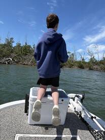 A young angler standing on a cooler, casting a line while fishing in a scenic waterway surrounded by mangroves.