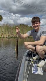 Young angler proudly holding a large fish while fishing in a scenic waterway, showcasing a successful catch.
