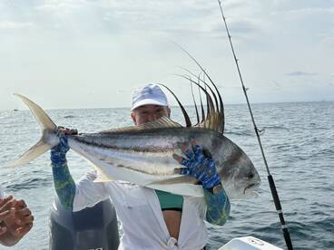 A proud angler displaying a large Roosterfish while fishing on a boat in open waters.