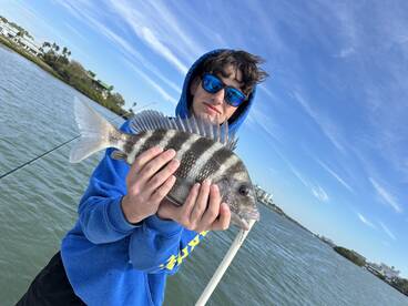 A young angler proudly displaying a striped Sheepshead fish while fishing in a coastal waterway.