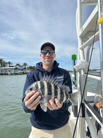 Angler proudly displaying a Sheepshead caught during a fishing trip, with a scenic waterfront in the background.