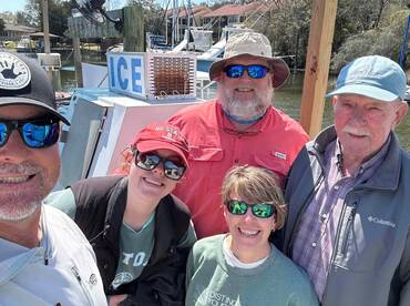 A cheerful group of anglers posing for a selfie on the dock, with a boat in the background, showcasing a fun day of fishing.