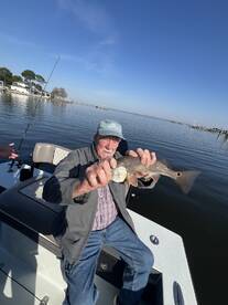 An elderly angler proudly displaying a Redfish while fishing from a boat in calm waters.