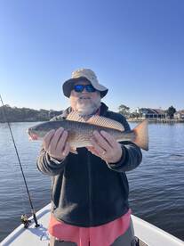 An angler proudly displaying a Redfish while fishing on a calm day, showcasing the serene waters and a beautiful backdrop.