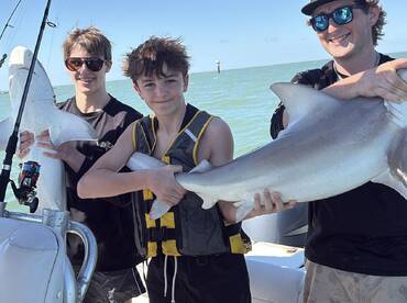 Two young anglers proudly displaying their catches of sharks while enjoying a day of fishing on the water.