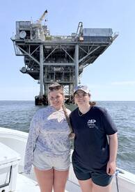 Two anglers posing in front of an offshore oil rig, enjoying a day on the water.