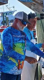 Two individuals engaged in a fishing-related activity at a dock, with boats visible in the background.
