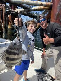 A young angler proudly displaying a striped fish while fishing near a structure, accompanied by an adult, showcasing a fun day on the water.