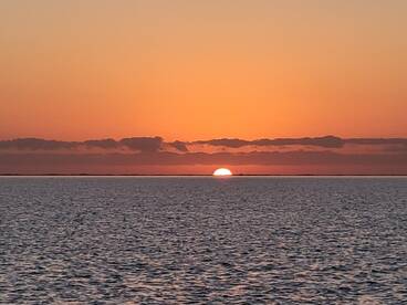 A serene sunset over the ocean, casting warm hues across the water, creating a tranquil fishing atmosphere.