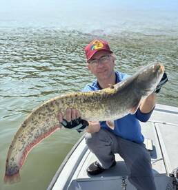 Angler proudly displaying a large Catfish while fishing on a calm waterway.