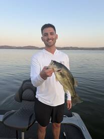 Angler proudly displaying a large Largemouth Bass while fishing on a serene lake at sunset.